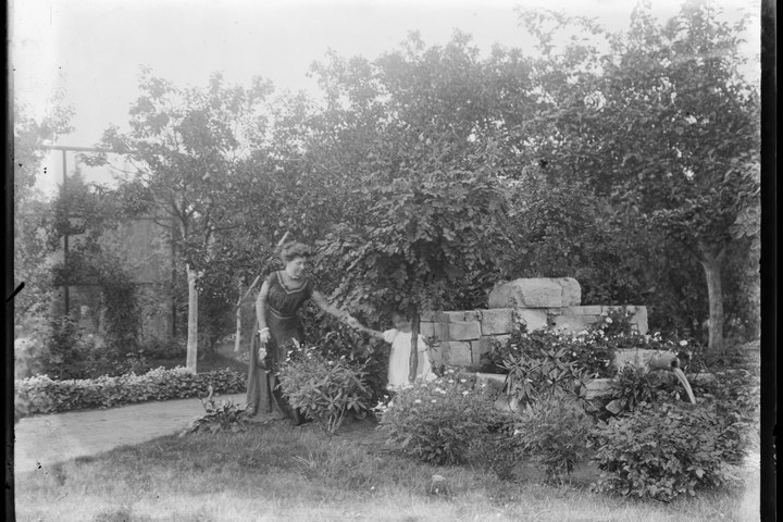 Glasnegatief van familiefoto waarop vrouw met kind in tuin