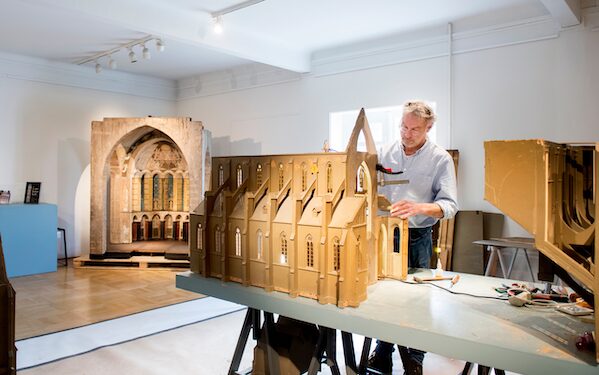 Foto van een man die werkt aan de restauratie van unieke kerkmaquettes