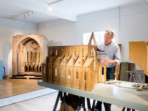 Foto van een man die werkt aan de restauratie van unieke kerkmaquettes